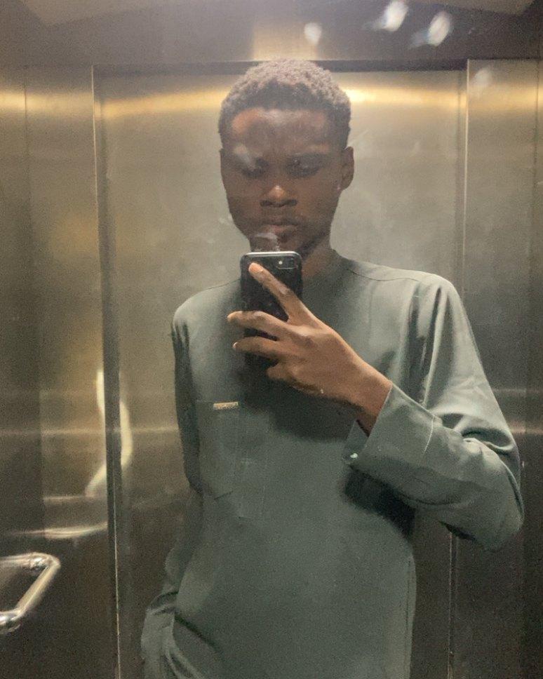 Oloyede Al-amin Oladapo taking a mirror selfie in a brushed-steel elevator, wearing a sage-green kaftan.